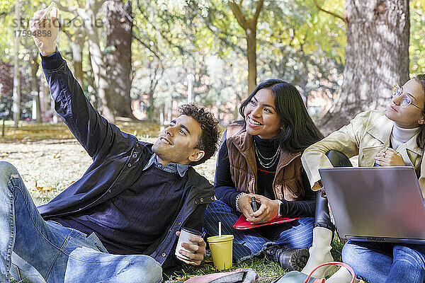 Lächelnder Mann  der im College-Park ein Selfie mit Freunden auf dem Smartphone macht