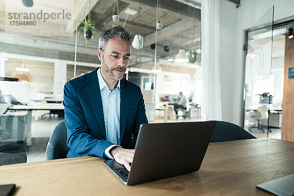 Selbstbewusster Geschäftsmann mit Laptop am Schreibtisch im Büro