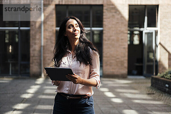Nachdenkliche Geschäftsfrau mit Tablet-PC steht auf Fußweg