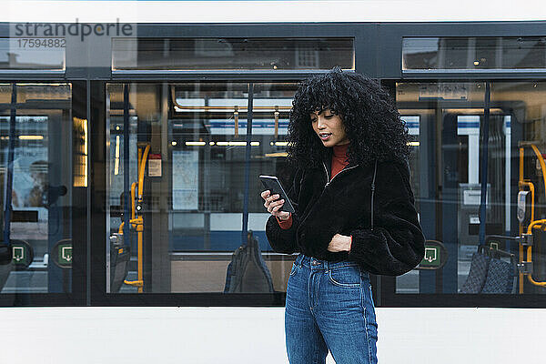 Modische junge Frau benutzt Smartphone vor der Straßenbahn