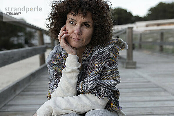 Nachdenkliche Frau sitzt im Winter auf einer Fußgängerbrücke