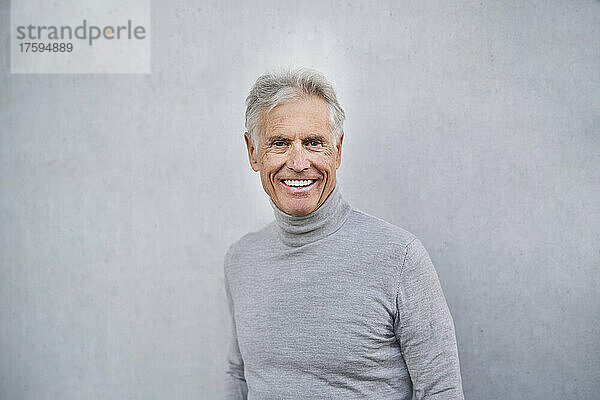 Smiling elderly man in front of gray wall