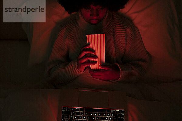 Junge Frau schaut sich Popcorn auf dem Laptop im Schlafzimmer an