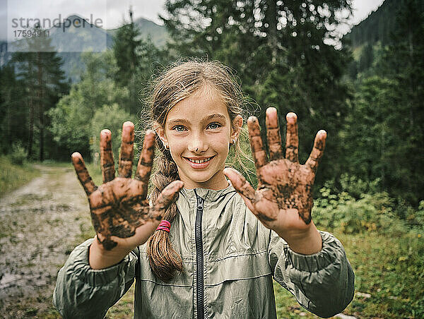 Lächelndes Mädchen zeigt schlammige Hände im Wald