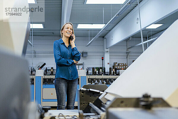 Glückliche Geschäftsfrau  die in der Fabrik auf dem Smartphone spricht
