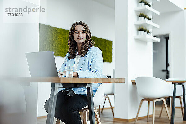 Schöne junge Geschäftsfrau mit Laptop sitzt am Schreibtisch im Büro