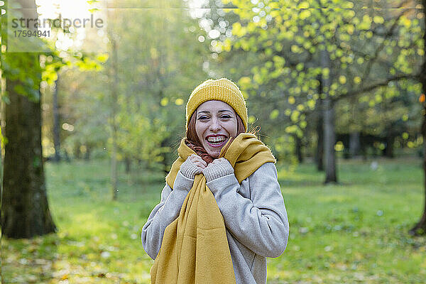 Fröhliche Frau mit gelber Strickmütze und Schal steht im Herbstpark