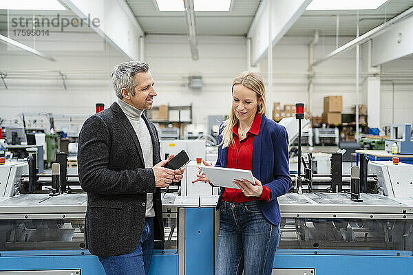 Lächelnder Geschäftsmann diskutiert mit Kollegen über Tablet-PC an Maschinen in der Fabrik