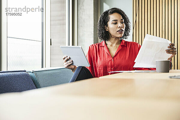 Junge Geschäftsfrau mit Tablet-PC prüft Dokumente im Büro