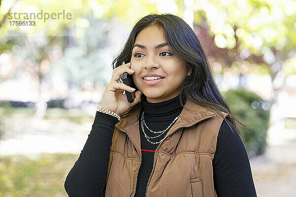 Junge Studentin spricht im College-Park mit dem Smartphone