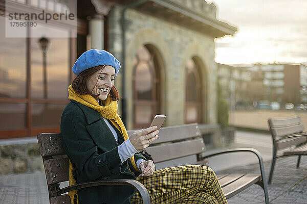 Lächelnde Frau  die mit ihrem Mobiltelefon im Internet surft und auf einer Bank sitzt