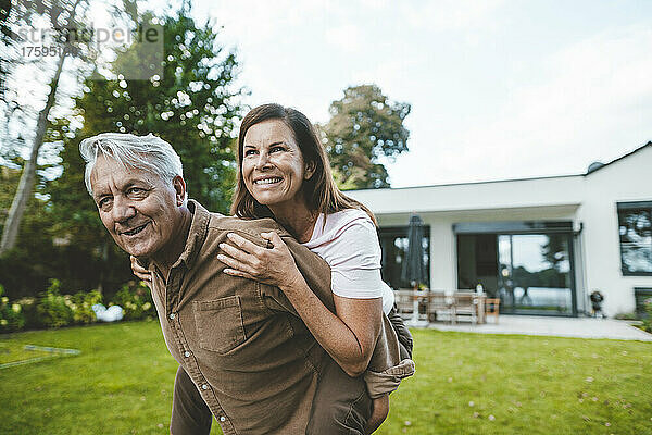 Glückliche Frau genießt die Huckepackfahrt  die ihr ein älterer Mann im Hinterhof gibt