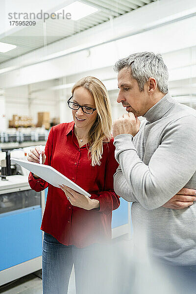 Geschäftsfrau mit Brille diskutiert über Tablet-PC mit Kollege in der Fabrik