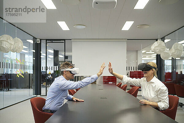 Fröhliche Geschäftsleute mit VR-Brille geben im Büro High-Five