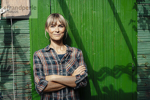 Blonde Frau mit verschränkten Armen vor grüner Wand