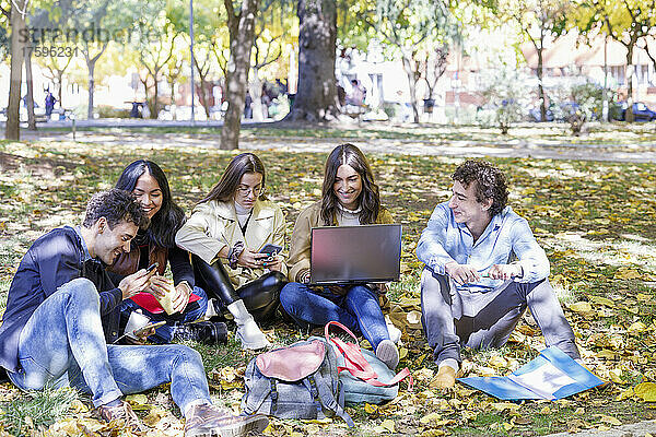 Zufriedene Studenten nutzen Smartphone und Laptop im College Park