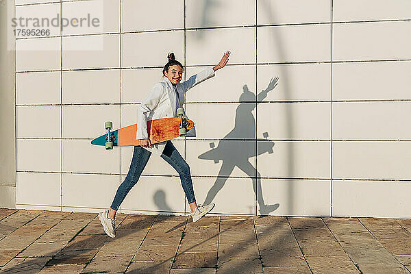 Fröhliche Frau springt mit Skateboard auf Fußweg