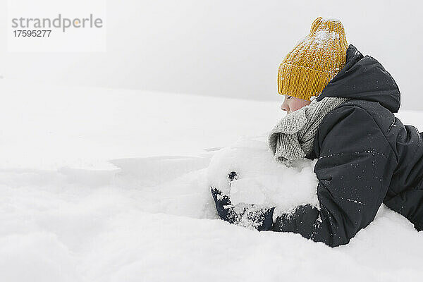 Boy wearing yellow knit hat playing with snow