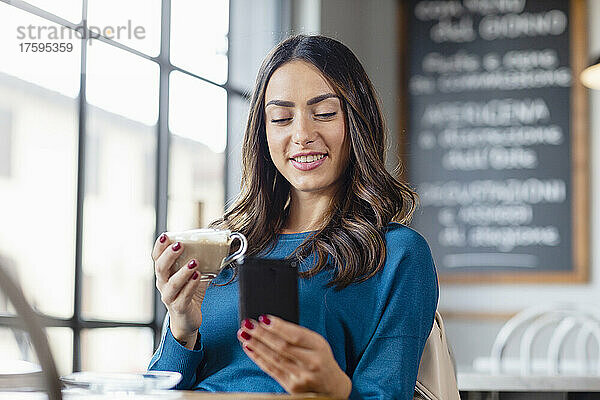 Junge Frau benutzt Smartphone und trinkt Cappuccino im Café