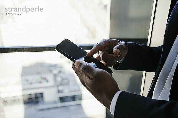 Geschäftsmann benutzt Smartphone am Fenster im Büro