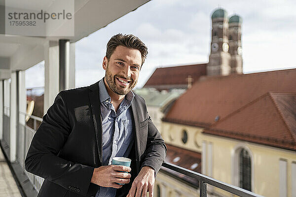 Lächelnder Geschäftsmann mit Kaffeetasse auf dem Balkon