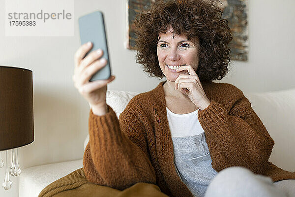 Glückliche Frau bei Videoanruf über Smartphone zu Hause