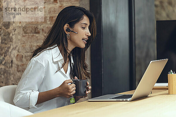 Geschäftsfrau mit Kaffeetasse diskutiert per Videoanruf im Coworking-Büro