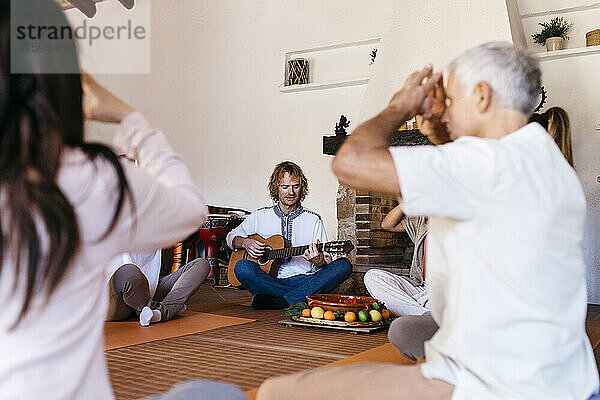 Musiker spielt Gitarre und Freunde meditieren gemeinsam im Bauernhaus