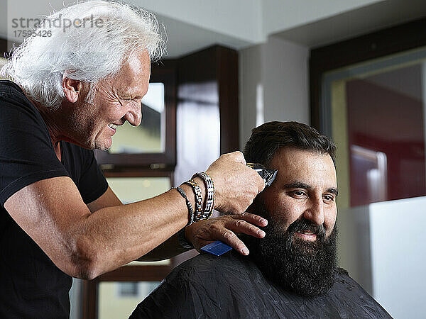 Lächelnder Friseur schneidet einem Mann im Salon mit einem Elektrorasierer die Haare