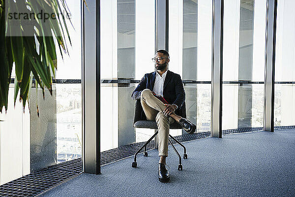 Geschäftsmann sitzt auf einem Stuhl neben dem Glasfenster im Büro