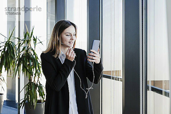 Berufstätige Frau nimmt im Büro an Videoanruf auf Smartphone teil
