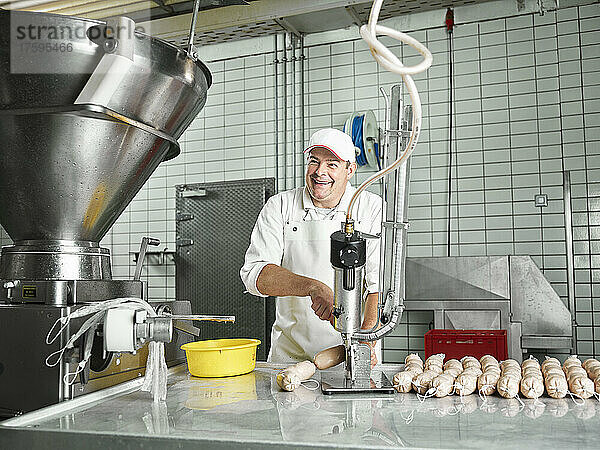 Happy butcher making sausages through machinery at factory