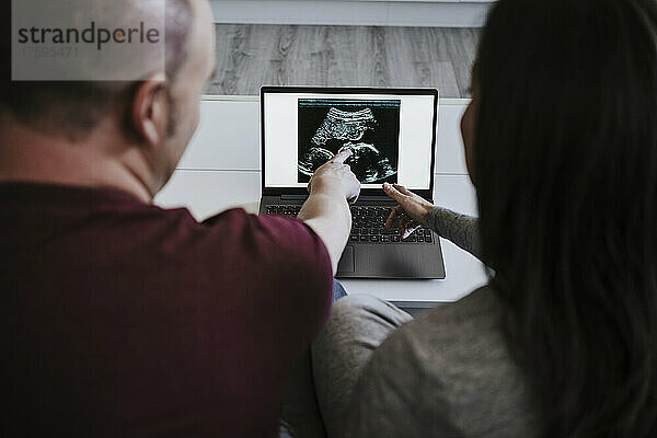 Mann und Frau schauen sich zu Hause Ultraschall auf dem Laptop an