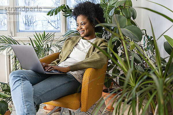 Lächelnde Geschäftsfrau  die zu Hause am Laptop neben Pflanzen arbeitet
