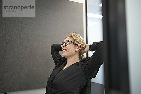 Lächelnde Geschäftsfrau mit den Händen hinter dem Kopf im Büro