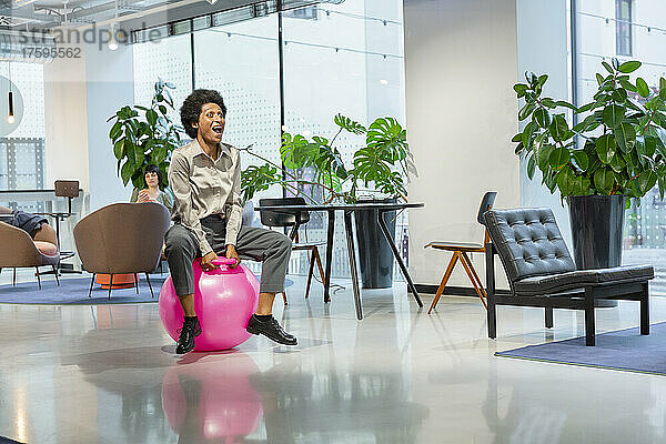 Fröhliche Geschäftsfrau sitzt auf einem Trichterball in der Lobby