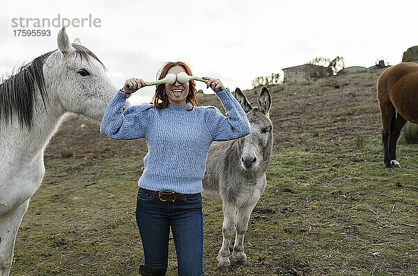 Frau bedeckt Augen mit Frühlingszwiebeln von Pferd und Esel auf einer Ranch