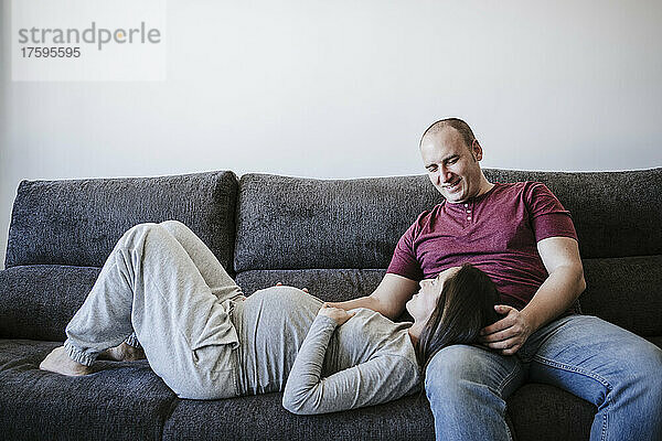 Schwangere Frau liegt zu Hause auf dem Schoß eines Mannes auf dem Sofa