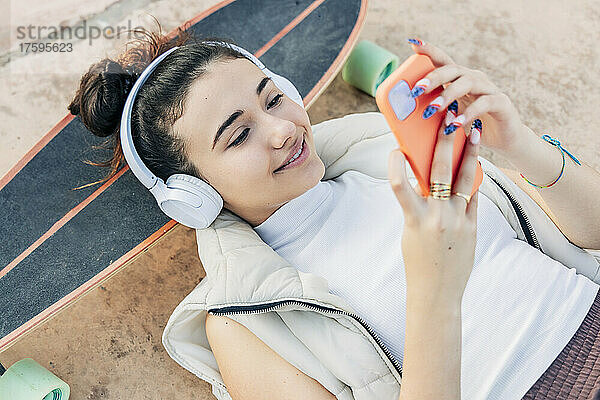 Frau mit Skateboard hört Musik über Kopfhörer und benutzt Smartphone