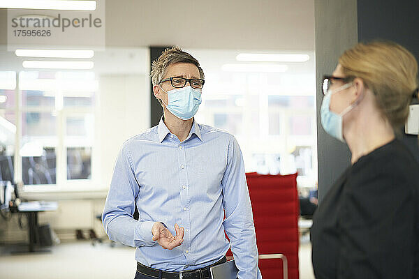 Geschäftsmann trägt schützende Gesichtsmaske und spricht mit Kollegen im Büro