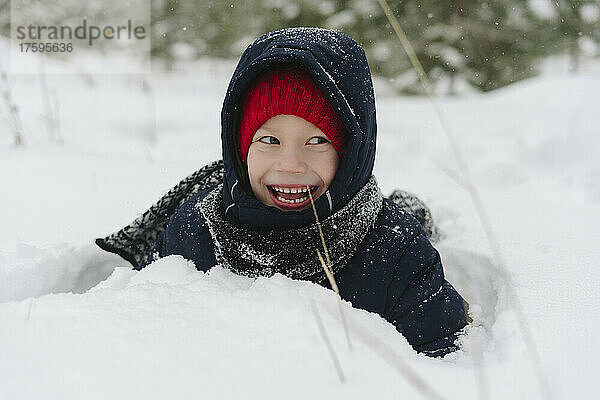 Fröhlicher Junge  der im Schnee im Wald spielt