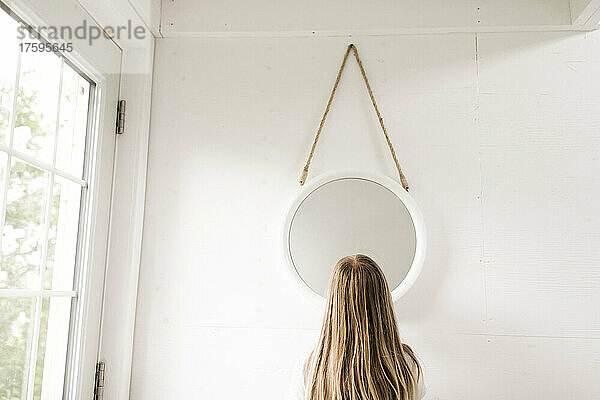 Blondes Mädchen steht zu Hause vor dem Spiegel