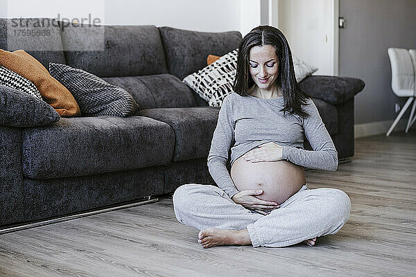 Lächelnde schwangere Frau sitzt zu Hause auf dem Boden