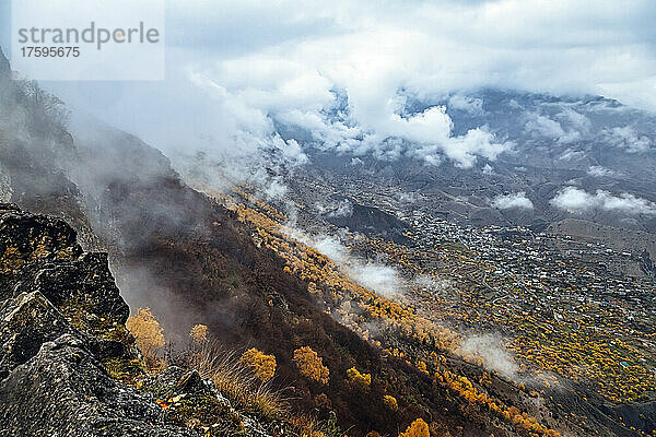 Russland  Dagestan  Gunib  niedrige Wolken über dem Kaukasus im Herbst mit einem Dorf im Hintergrund