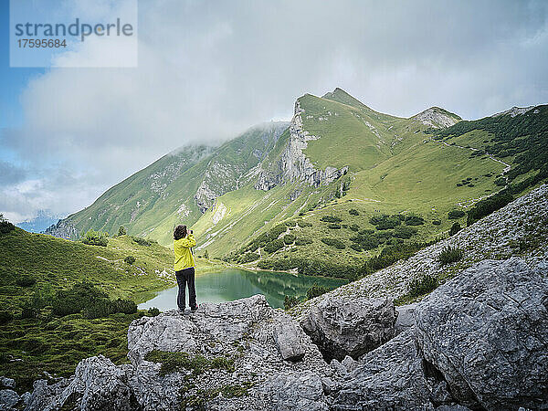 Frau steht auf einem Felsen und fotografiert Berge