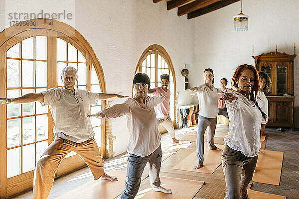 Gemischtrassige Freunde üben Kriegerposition im Yoga-Studio