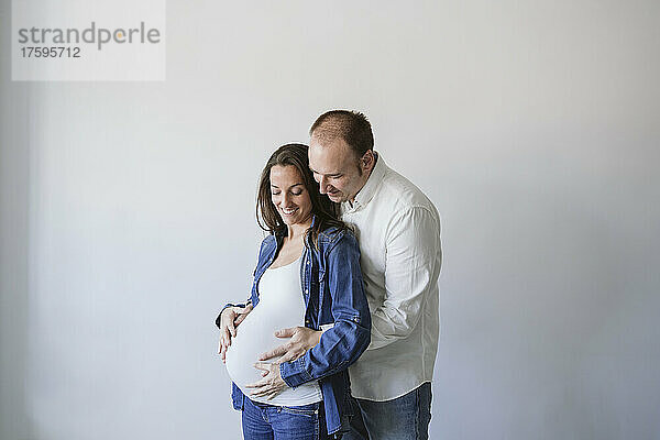Mann umarmt glückliche schwangere Frau an der Wand