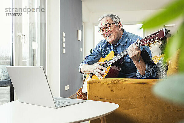 Älterer Mann lernt Gitarre durch Online-Tutorial auf dem Laptop zu Hause