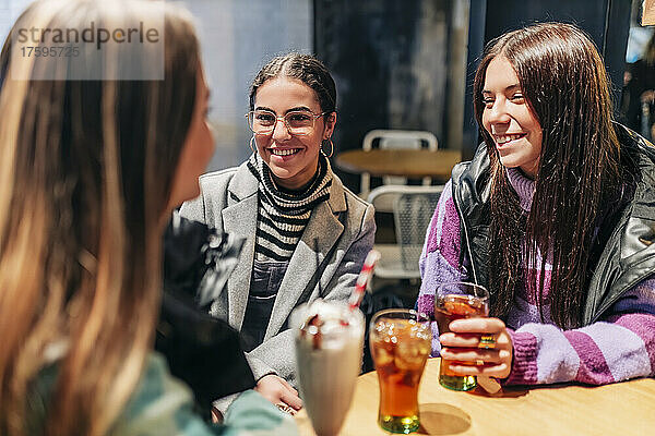 Lächelnde Frauen unterhalten sich mit jungen Freunden im Café