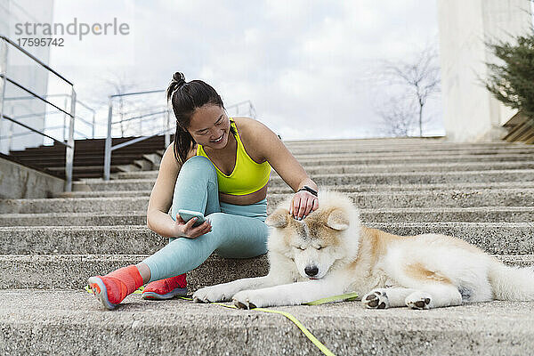 Young woman stroking Akita dog on staircase in park